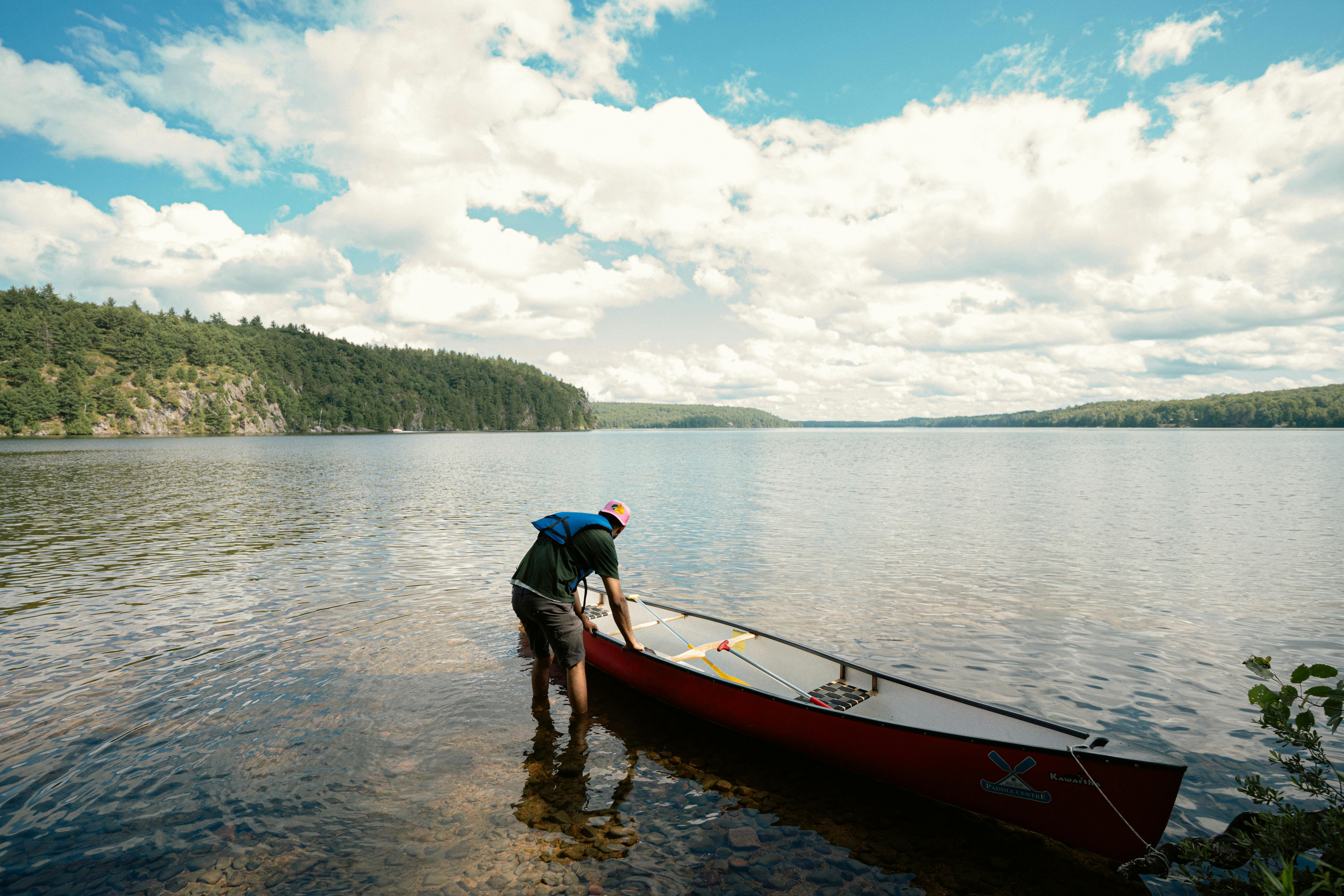 Man launching red canoe on a clear day at a serene lake in Ontario, Canada.
