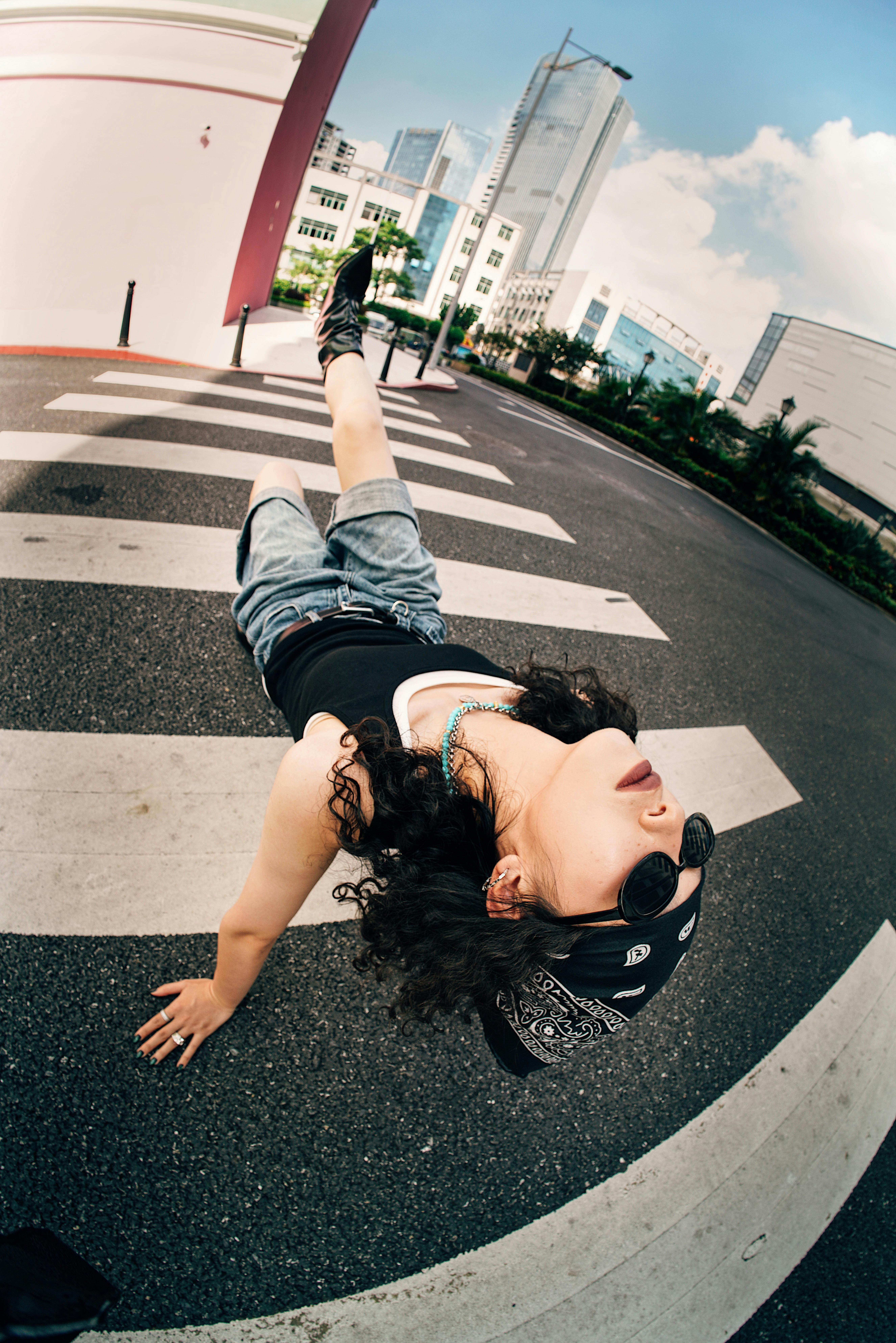 Stylish woman in bandana and sunglasses posing on a city crosswalk with a relaxed vibe.