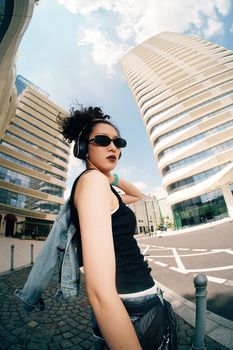 Young woman with headphones in a stylish urban area with modern skyscrapers in the background.