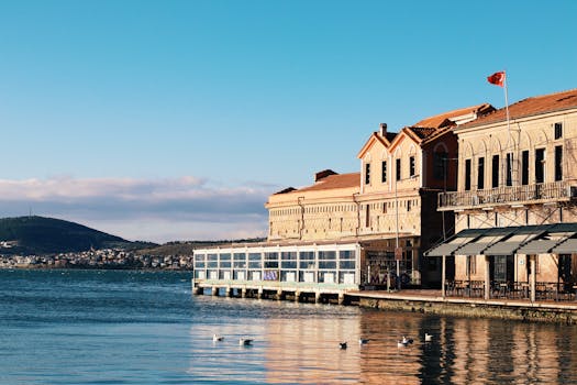 Scenic view of a waterfront building in Ayvalık, Turkey, bathed in sunlight with a clear blue sky.