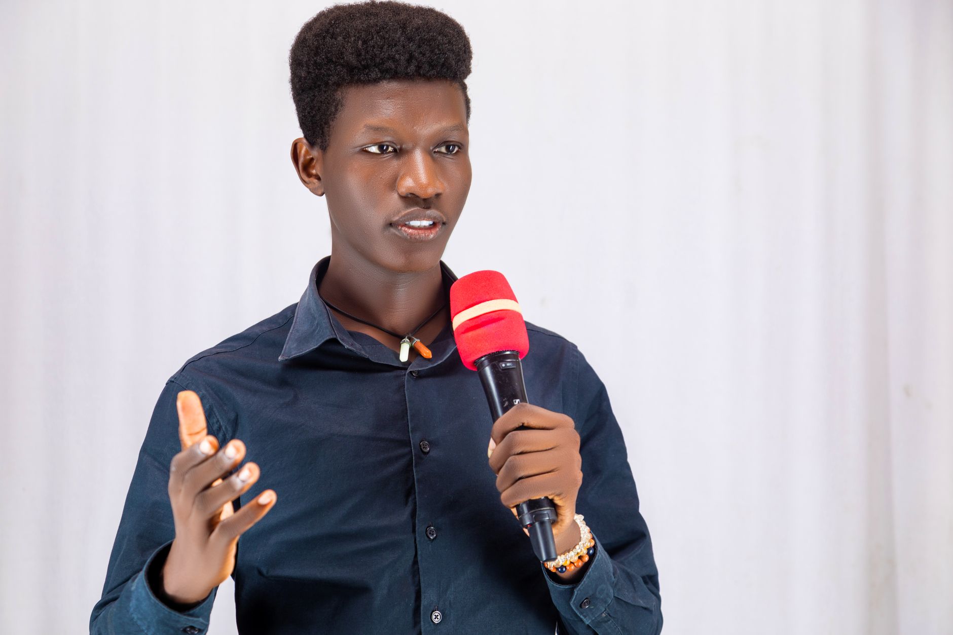 Confident young man presenting with a red microphone, wearing a dark shirt indoors.