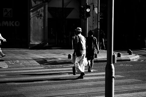 Free Dynamic black and white street photo showing people crossing in urban sunlight shadows. Stock Photo