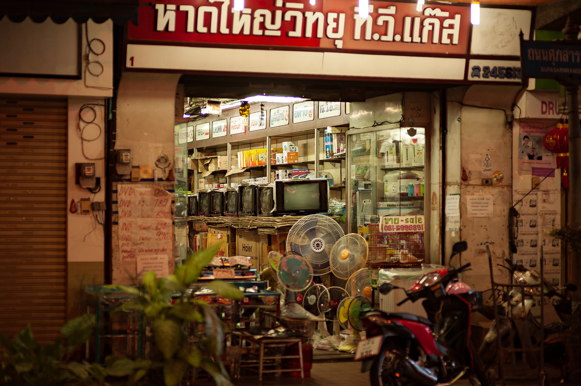 A well-lit vintage electronics store with retro TVs and fans on display, viewed from the street.
