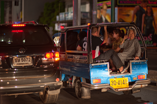Busy street scene at night with people seated in a blue pickup truck taxi.