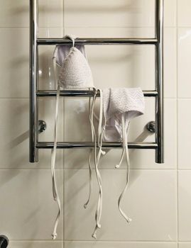 White bikini drying on a chrome towel rack in a tiled bathroom setting.