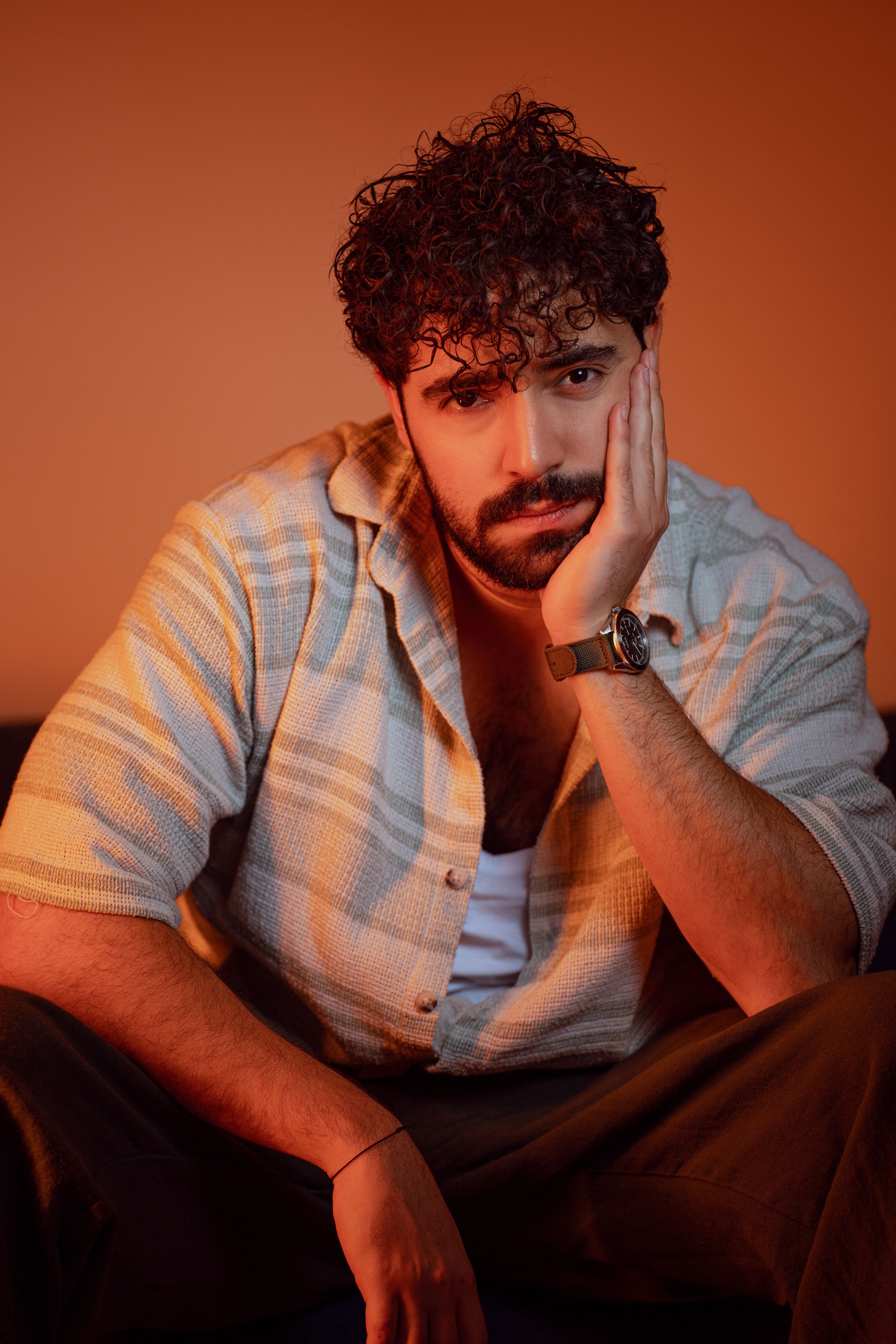 Portrait of a bearded man with curly hair in warm lighting, exuding a fashionable and introspective vibe.