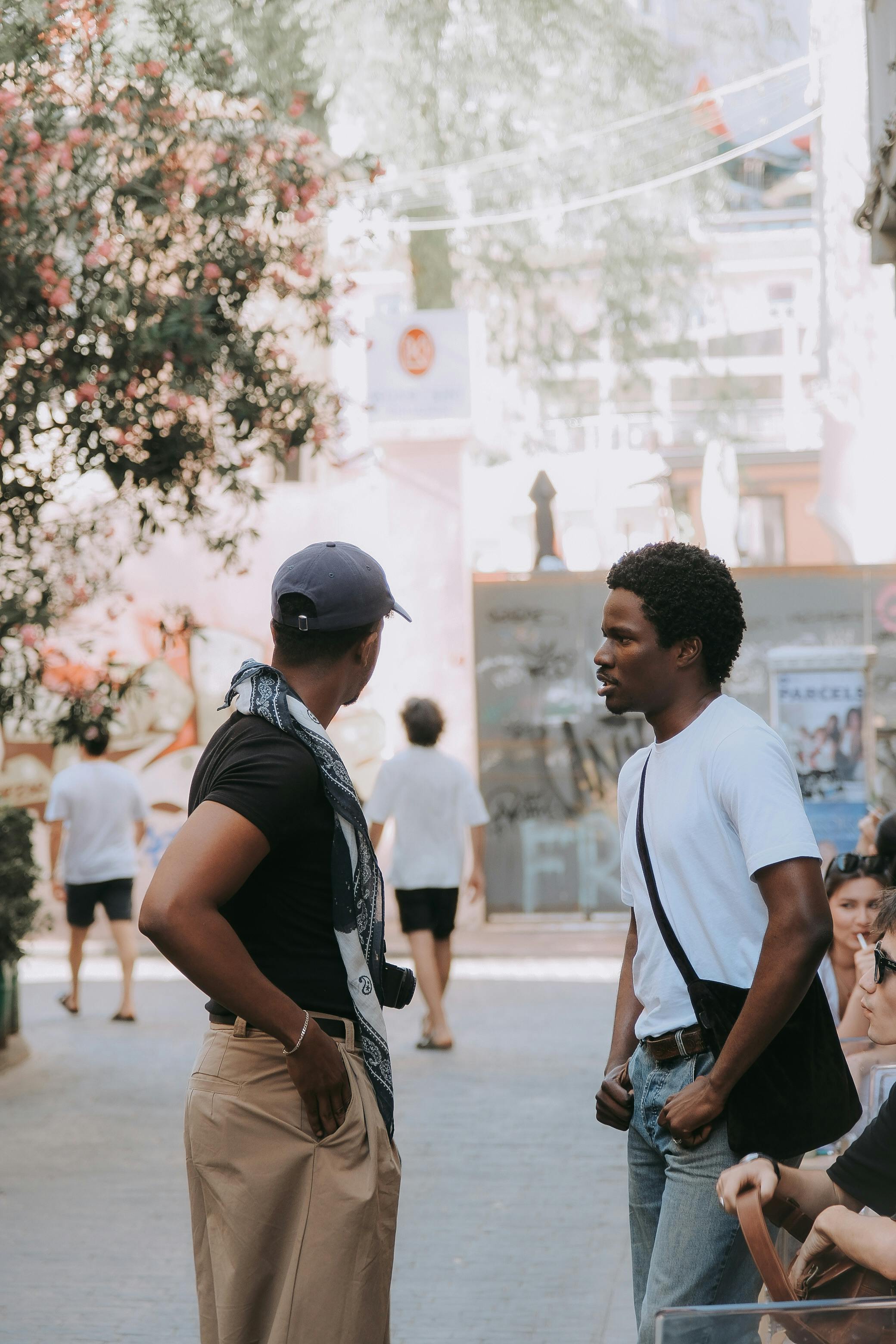 Two men having a conversation in a lively urban alley, surrounded by people and vibrant cityscape.