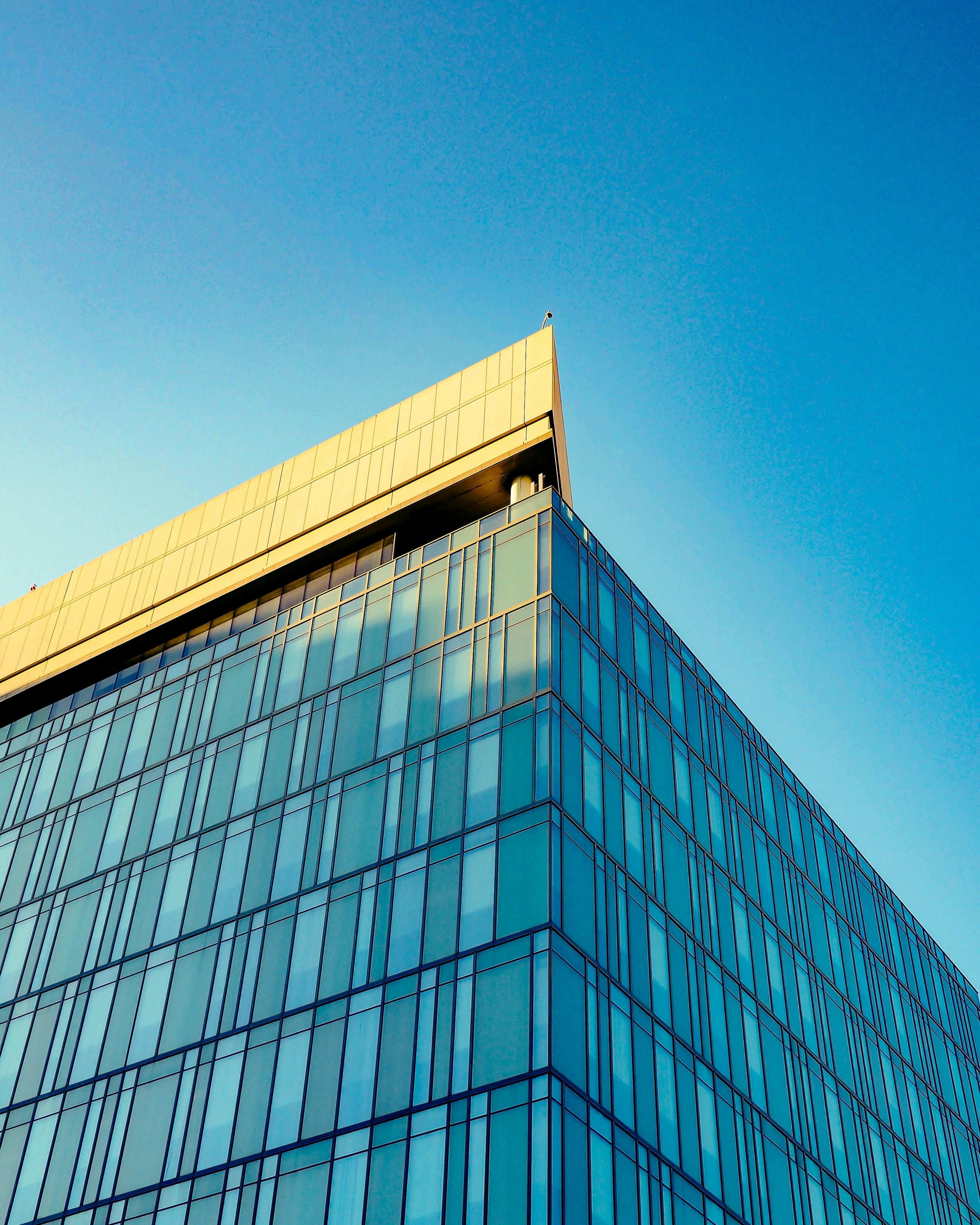 A sleek modern glass building under a vibrant blue sky. Captivating architectural design.