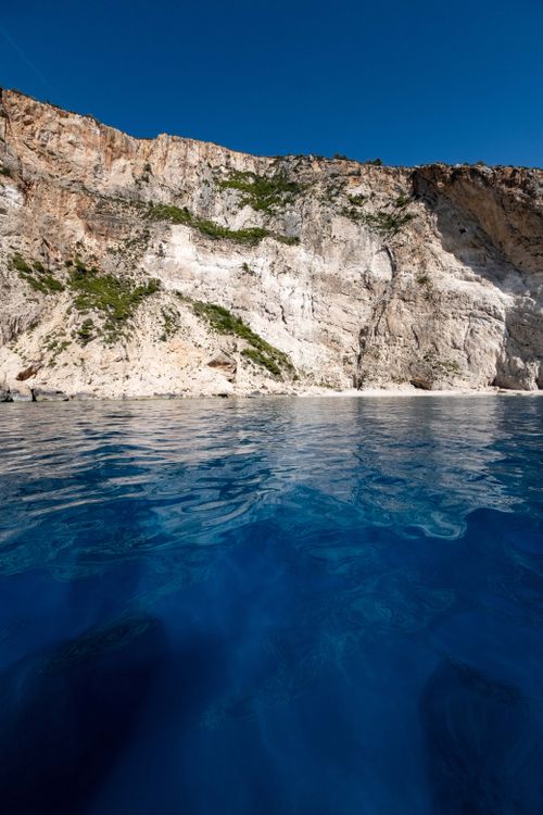 Free A stunning view of rugged cliffs against a clear blue sky and vibrant ocean waters. Stock Photo