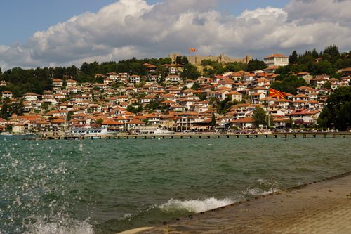 Free Charming view of Ohrid's waterfront with traditional houses and a historic fortress under a cloudy sky. Stock Photo