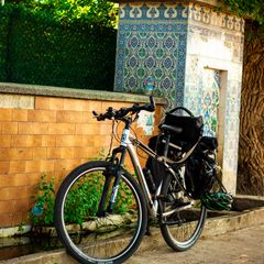 Bike loaded with black rear panniers and a black rack-top bag, leaning on an orange tiled wall under trees