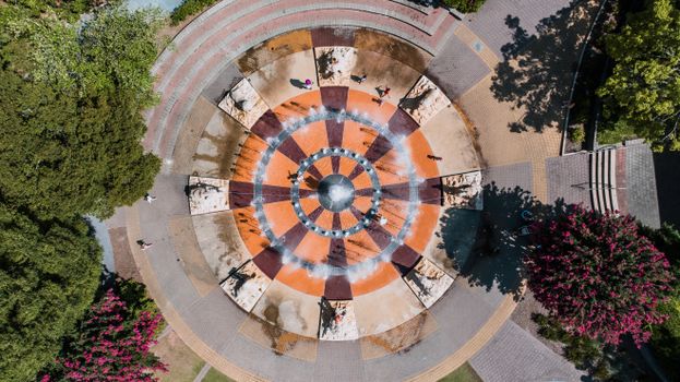Aerial shot of a vibrant circular fountain surrounded by greenery in a public park.