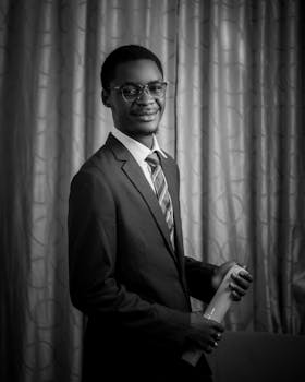 Black and white portrait of a young man in a suit holding a diploma, exuding elegance and achievement.