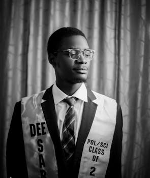 Portrait of a young graduate wearing a formal suit and glasses, looking to the side.