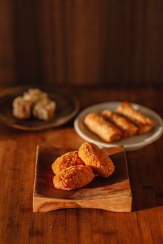 Delicious fried snacks including croquettes, spring rolls, and more on wooden plates, set against a warm, rustic background.