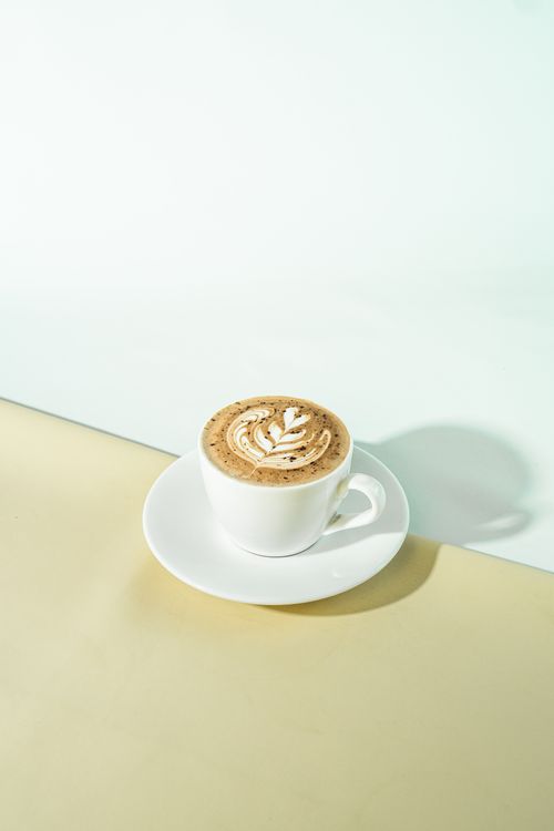 Free A minimalist photo of a cup of coffee with latte art on a white saucer against a beige background. Stock Photo