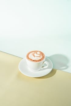 Artistic cappuccino with latte art on a saucer in a bright, minimalist café setting.