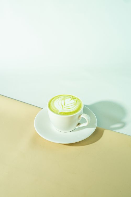 Free An artistic matcha latte with intricate foam design in a white cup on a pastel backdrop. Stock Photo