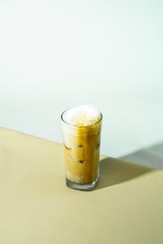 Tall glass of iced coffee with creamy foam on a neutral background.