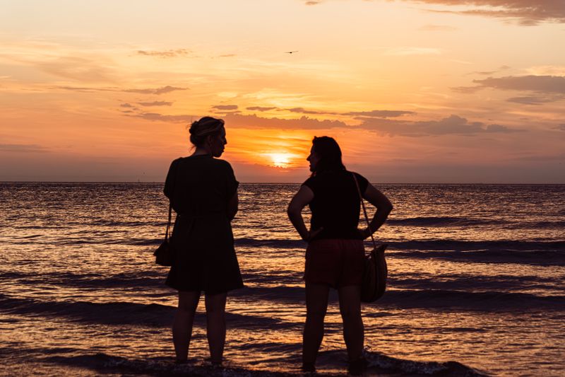 Two women enjoy a scenic sunset at Middelkerke Beach, Belgium, with a warm glow and peaceful ambiance.