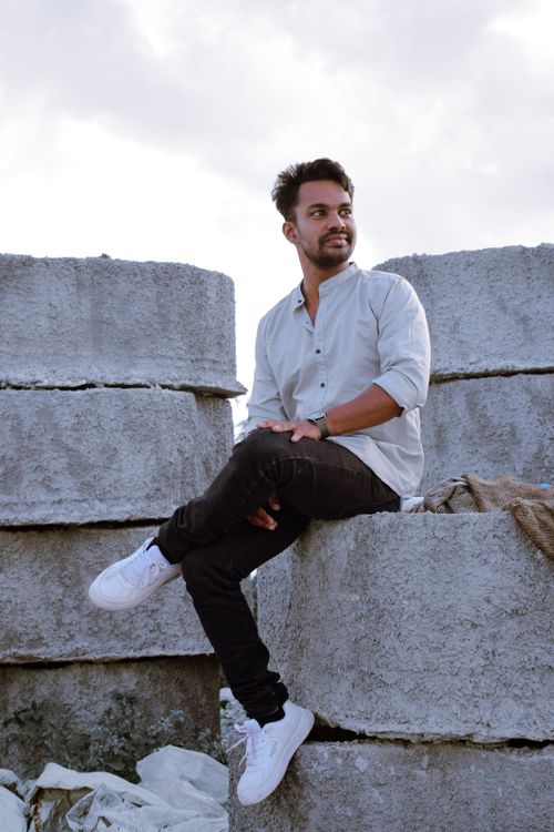 Free Young man sitting on concrete blocks, smiling outdoors. Stylish urban portrait. Stock Photo