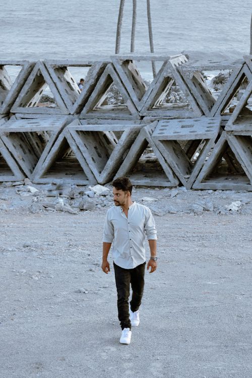 Free A man walking near large geometric structures on a coastal industrial site. Stock Photo