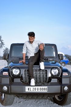 Young man poses on black SUV on a sunny day, embracing adventure and style.