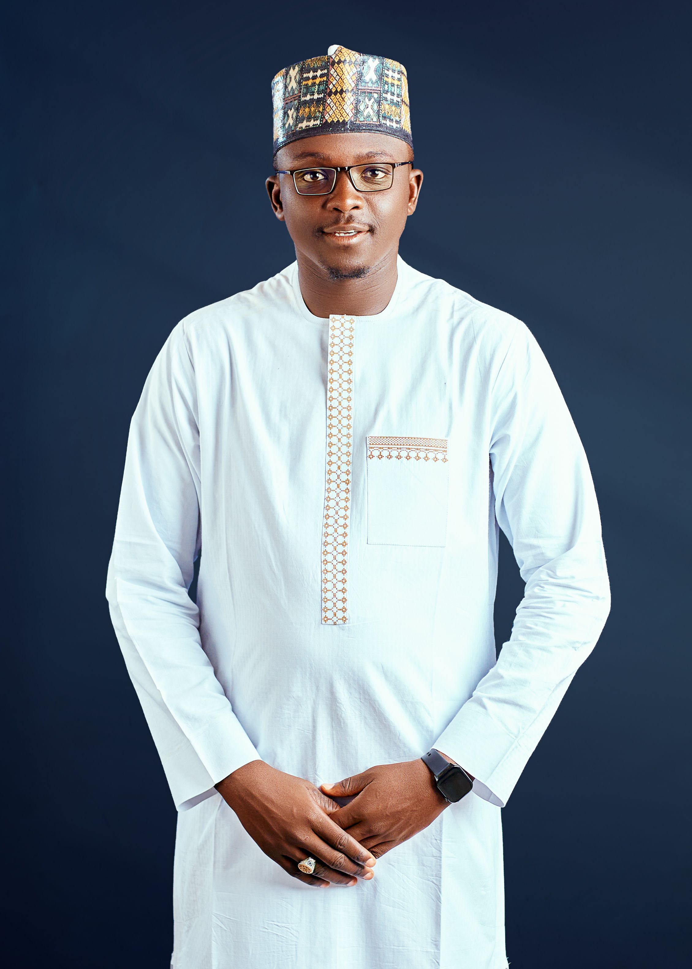 Portrait of a man in traditional African attire with a confident smile and glasses.