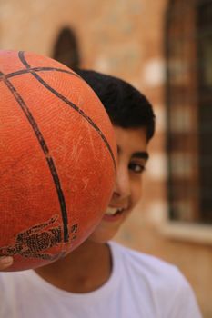 Teen boy holding a basketball in a sunny outdoor setting. Fun and sporty theme.
