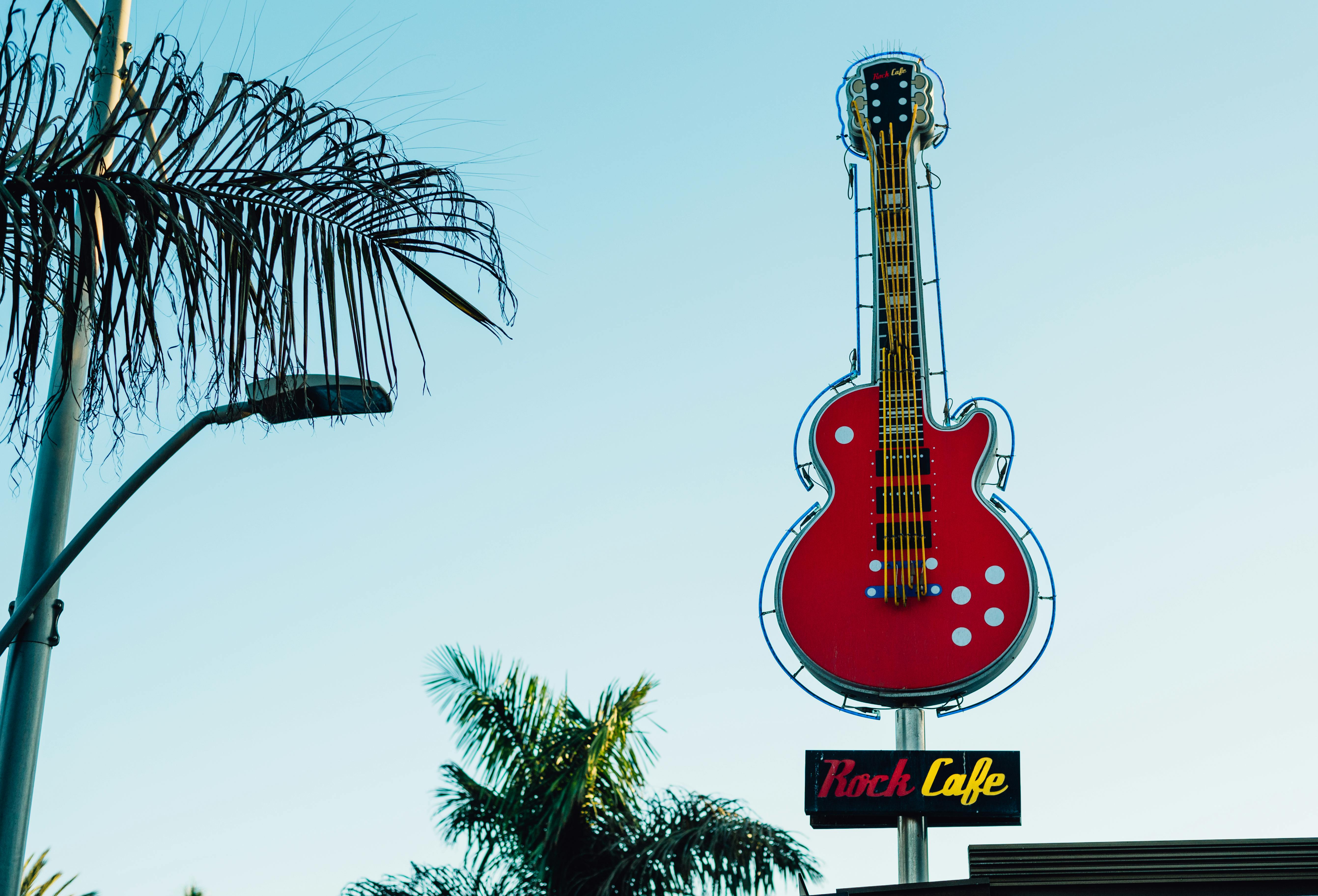 A bright red guitar sign at Rock Cafe with tropical palm trees and clear skies.
