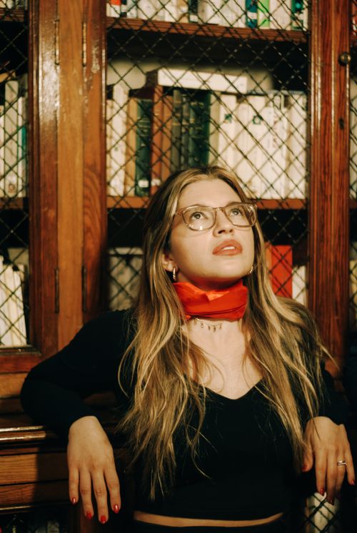 Free A woman with glasses and red scarf looks upwards in a library setting. Stock Photo