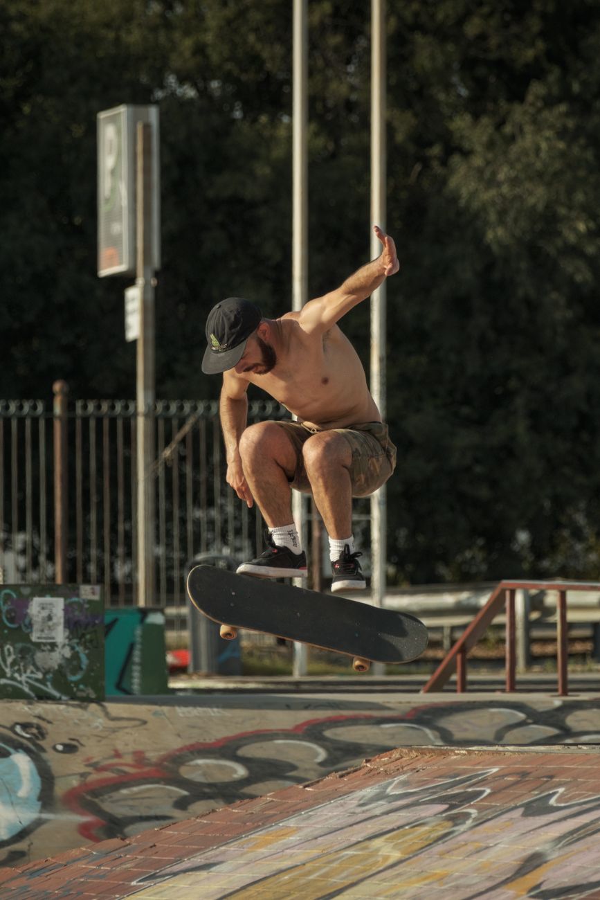 Shirtless skateboarder mid-air performing a trick at an outdoor skatepark, showcasing agility and skill.. shirtless, skateboa