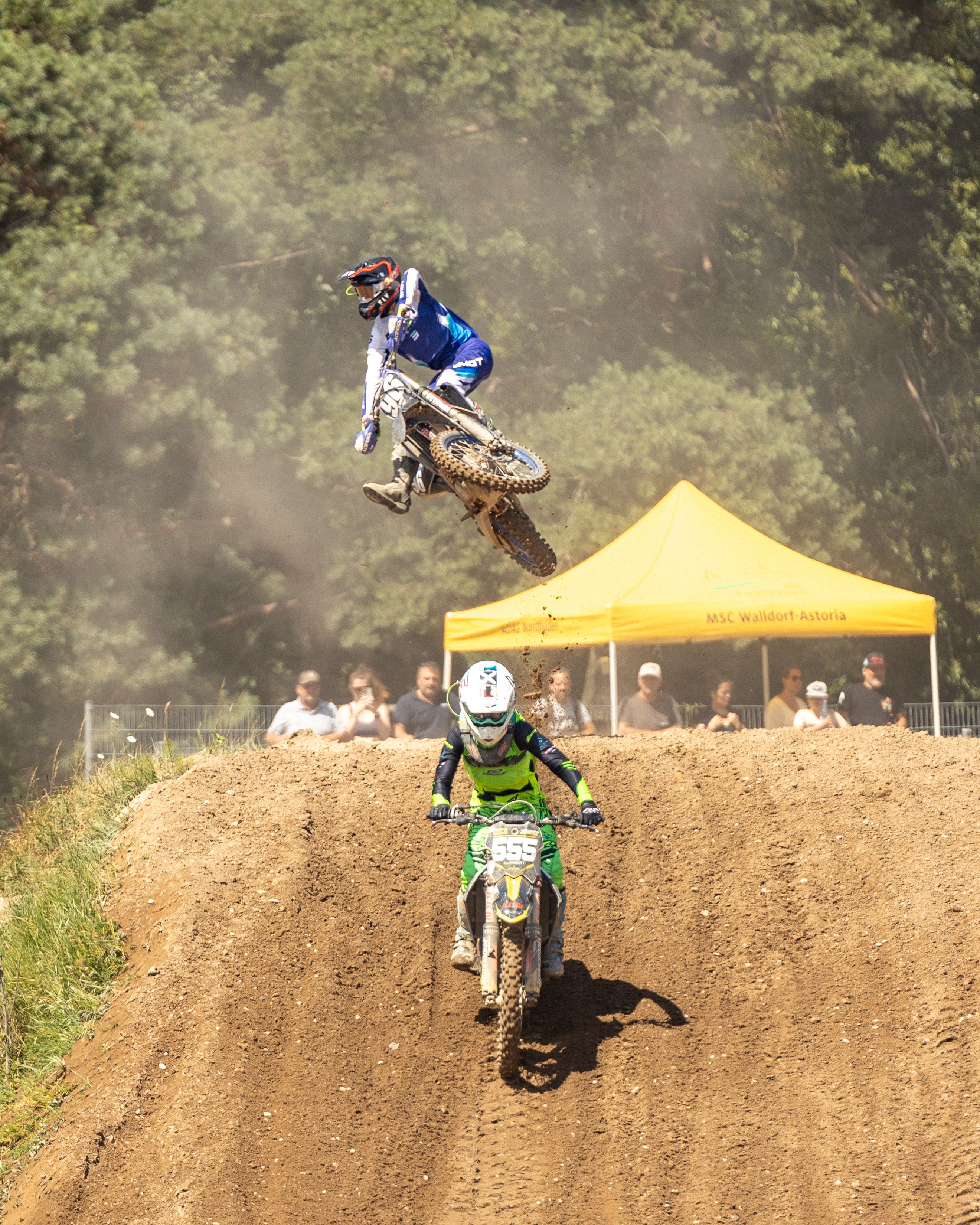 Dynamic motocross action with riders performing jumps on a sunlit dirt track.