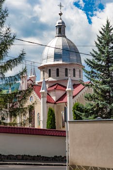 Beautiful church with a dome and red roof amidst trees under a blue sky.