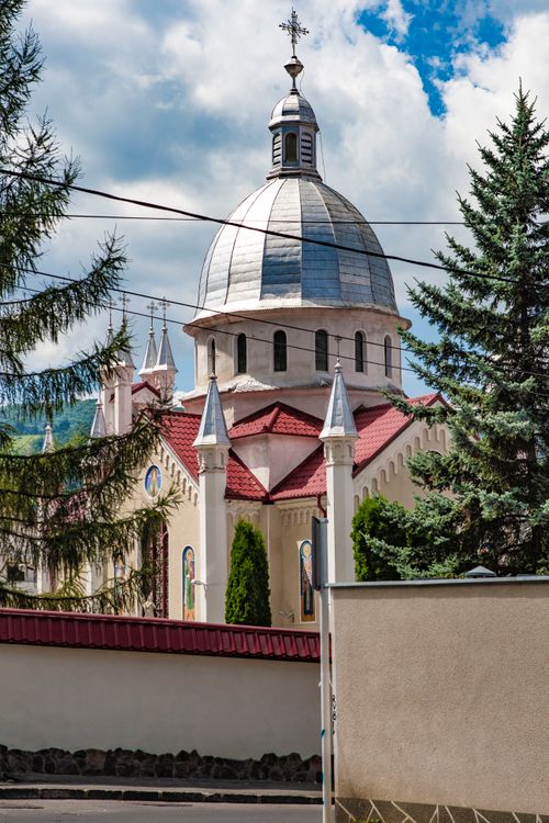 Free Beautiful church with a dome and red roof amidst trees under a blue sky. Stock Photo