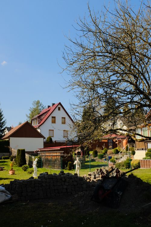 Free A peaceful garden with statues, trees, and houses under a clear blue sky. Stock Photo