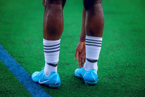 Free Athlete stretching on green field in blue cleats and striped socks, preparing for game. Stock Photo