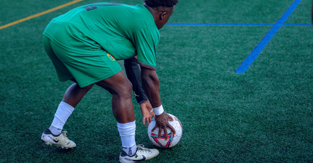 Football player in green uniform on grass field preparing to play, focusing on ball handling.