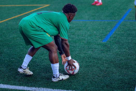 Football player in green uniform on grass field preparing to play, focusing on ball handling.