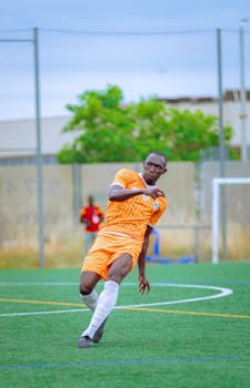 Soccer player in orange uniform on field mid-action during daytime match.