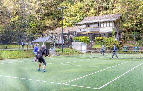 Free Four adults playing tennis on an outdoor court with a rustic house in the background. Stock Photo