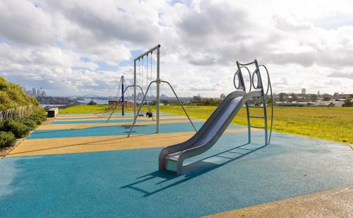Free Sunny day in a playground with a slide and swings overlooking city skyline. Stock Photo