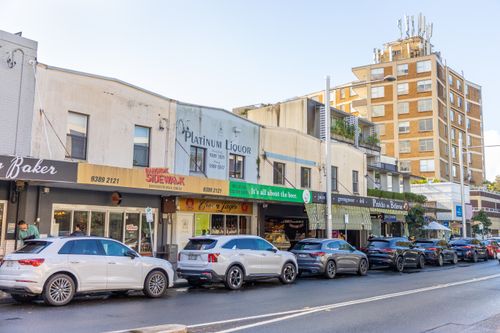 Free Lively urban street scene with parked cars and row of shops on a bright day, showcasing local businesses Stock Photo