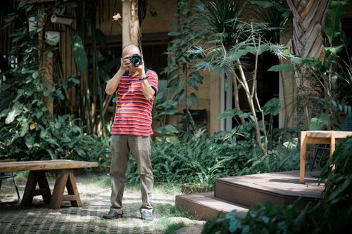 Free A man photographs outdoors surrounded by lush greenery in a cozy backyard. Stock Photo