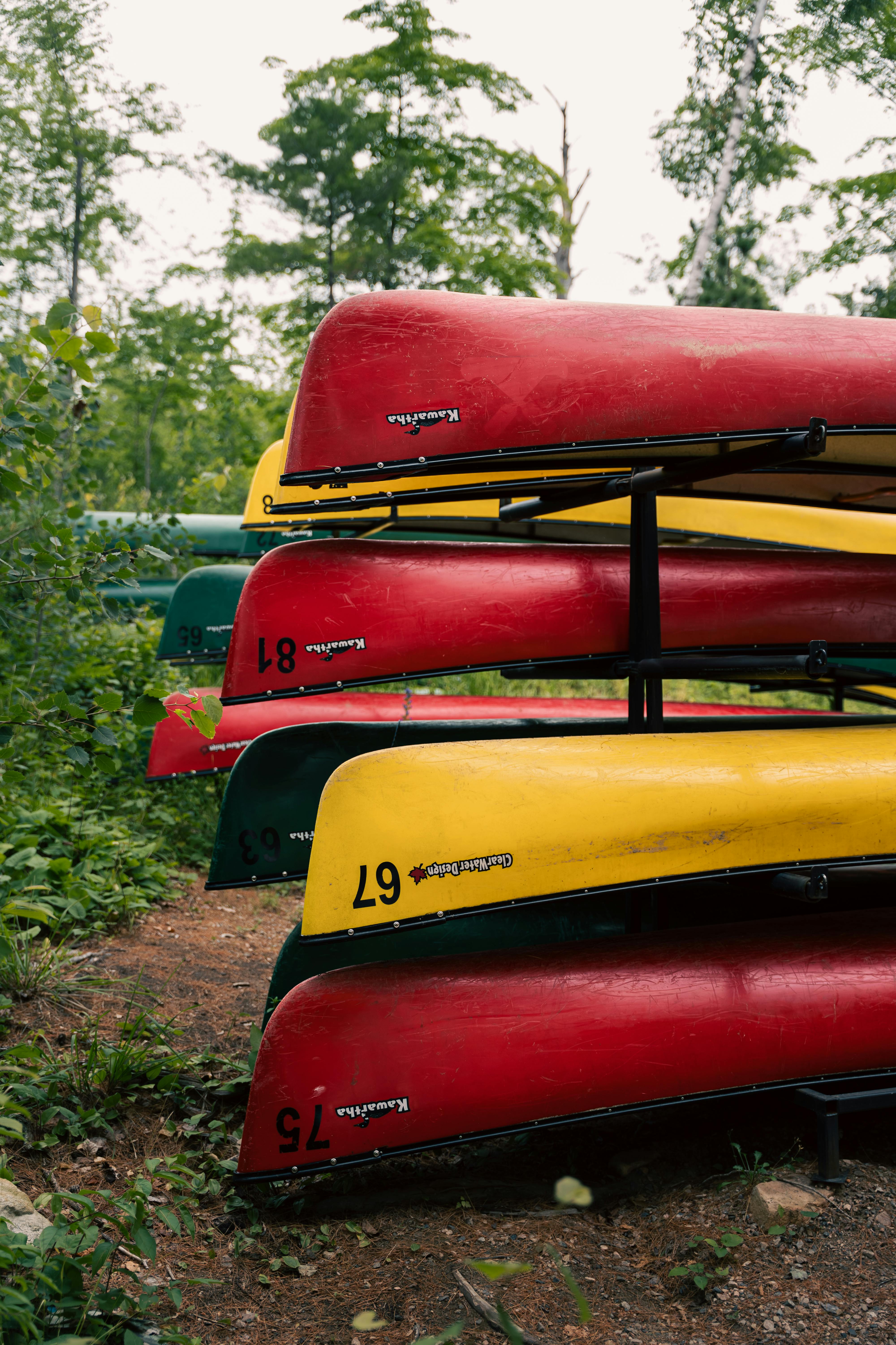 Vibrant red and yellow canoes stacked outdoors in a lush green forest, ideal for adventure.
