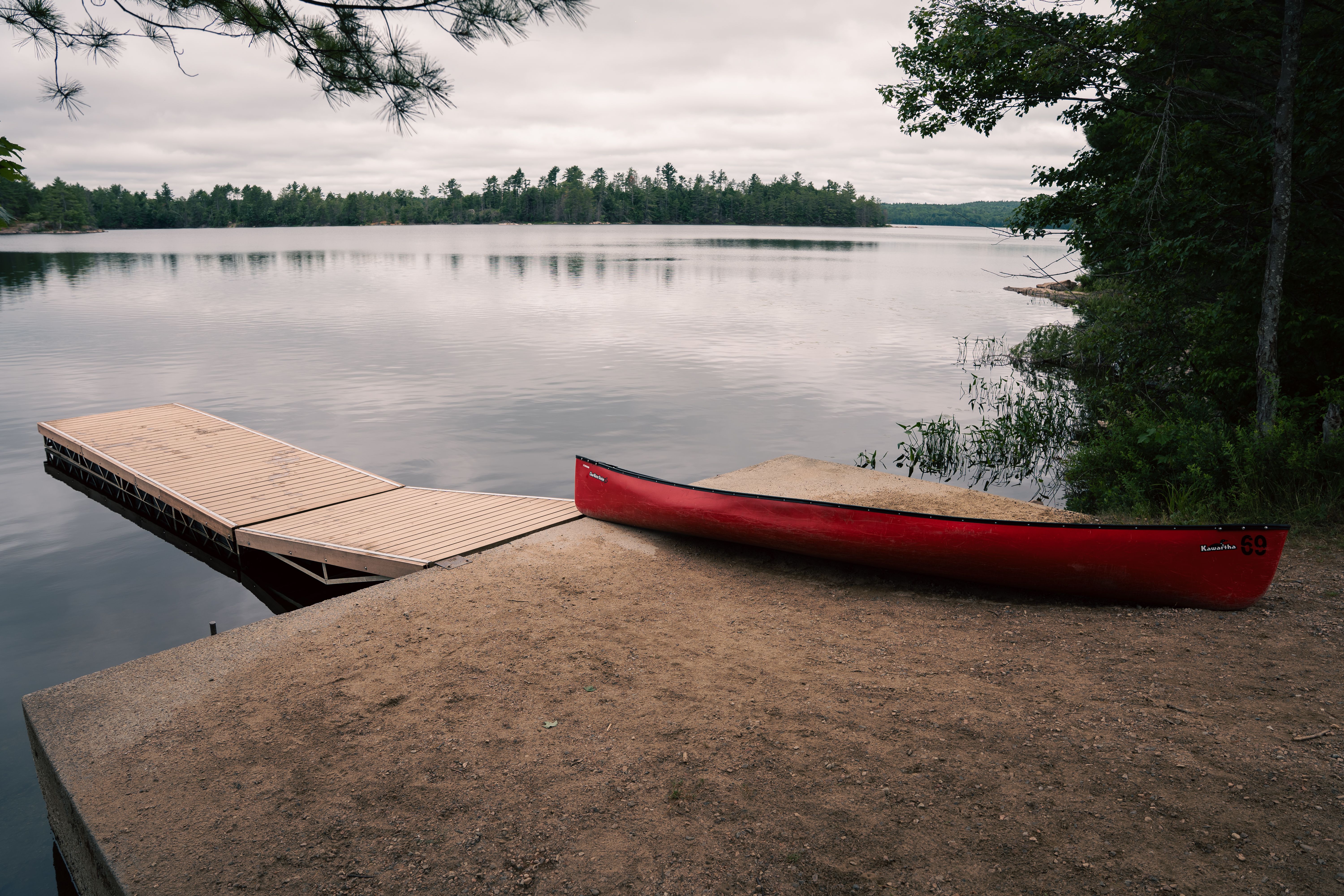 Serene Lakeside View with Red Canoe and Dock · Free Stock Photo
