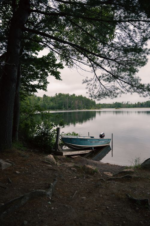 Free Tranquil lake view with docked boat surrounded by lush trees in Cloyne, Ontario. Stock Photo
