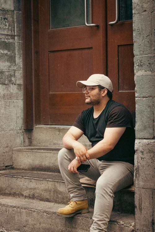 Free Casual man with cap sitting on steps, urban setting. Stock Photo