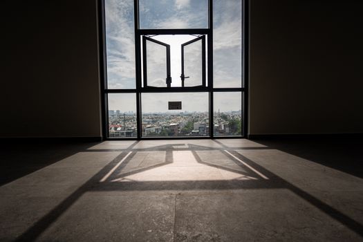 Sunlit room with open window framing a panoramic urban landscape view.