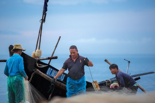 Free Image of fishermen handling nets on a traditional wooden boat at sea during daytime. Stock Photo